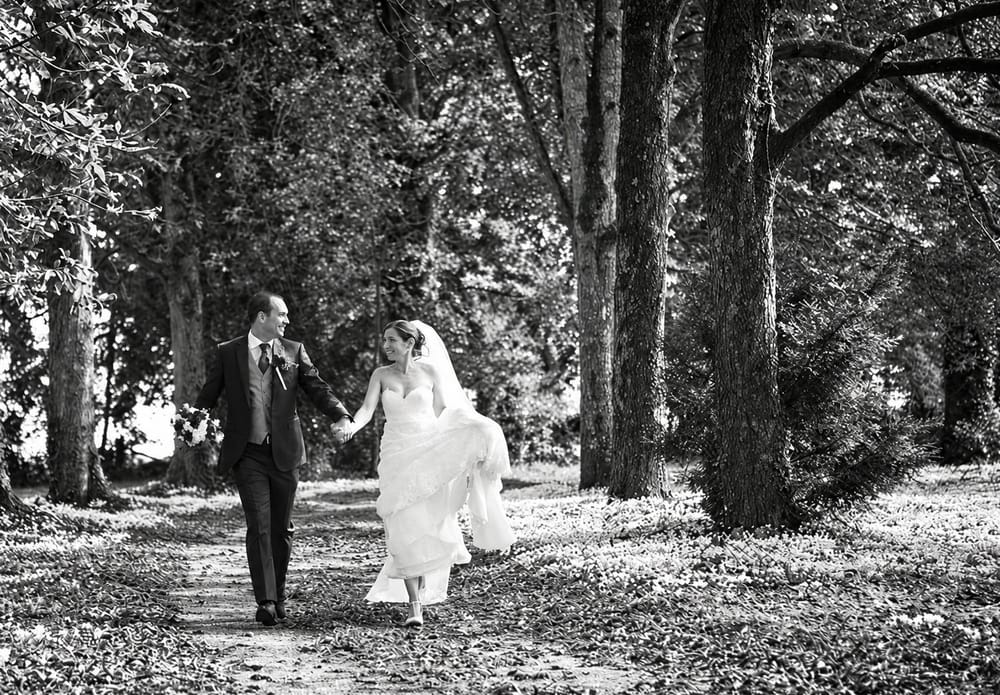 Les mariés se promènent main dans la main dans une allée d'arbres