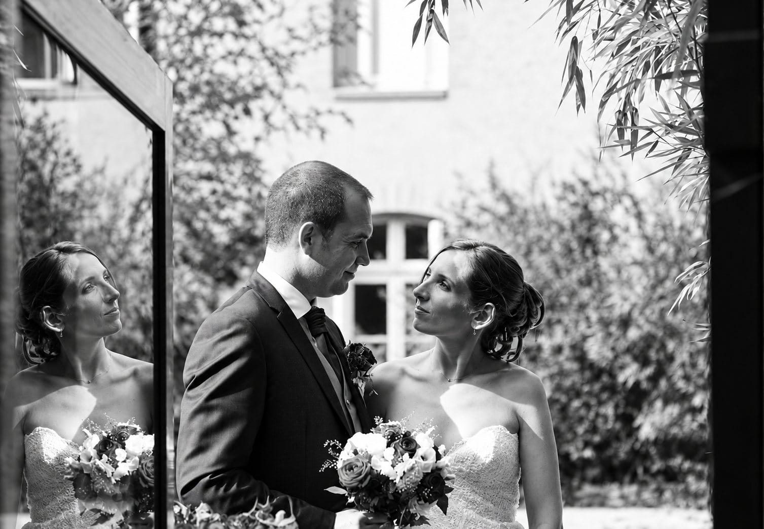 Les mariés posent avec leur bouquet devant une fenêtre